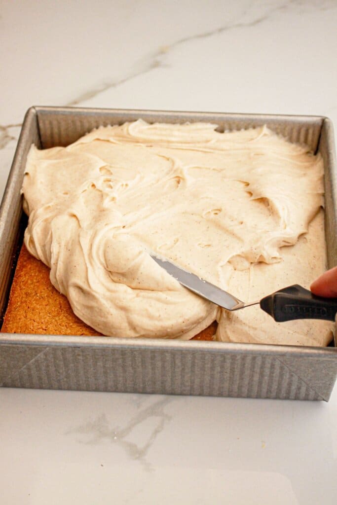 Cream cheese frosting being spread on bars in a baking dish.