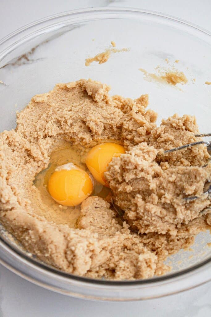 Eggs being added to dough in a glass bowl.