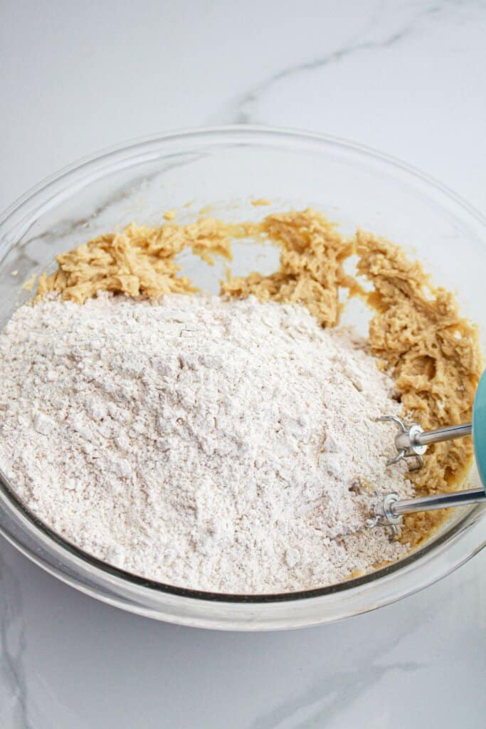 Flour being added to dough in a glass bowl.
