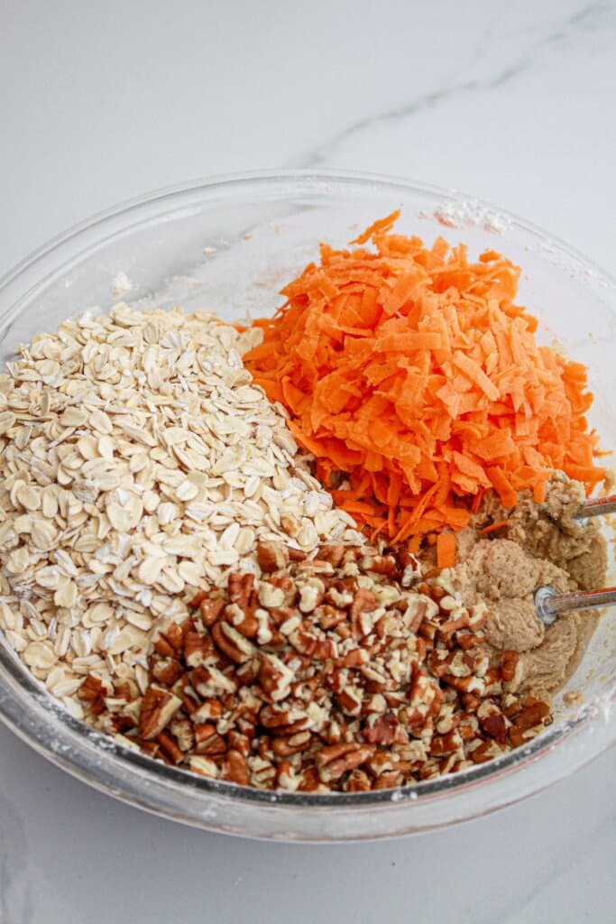 Carrots, pecans, and oats being added to a glass bowl.