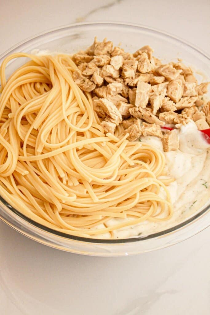 Spaghetti and chicken being added to creamy sauce in a large bowl.