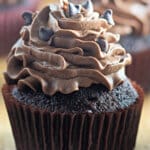 Chocolate buttercream cupcakes on a wooden cutting board.