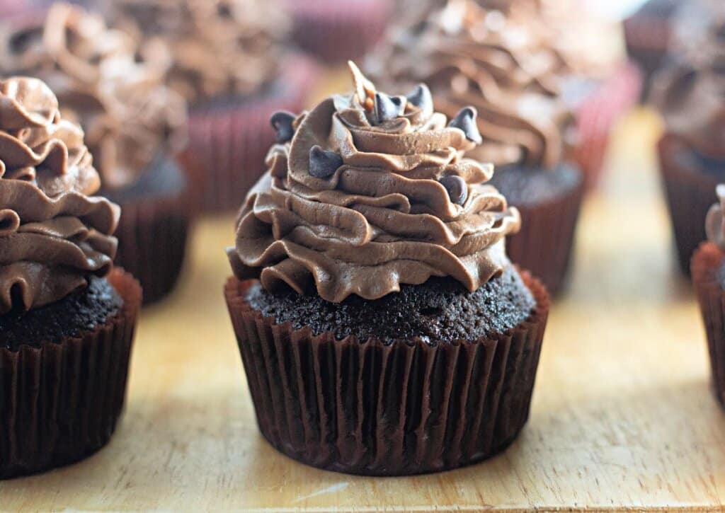 Chocolate buttercream cupcakes on a wooden cutting board.
