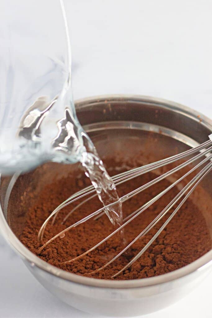 Boiled water being added to dry ingredients in a mixing bowl.