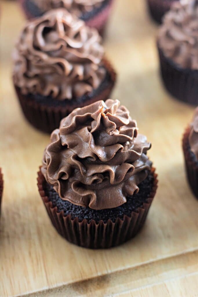 Chocolate buttercream cupcakes on a wooden cutting board.