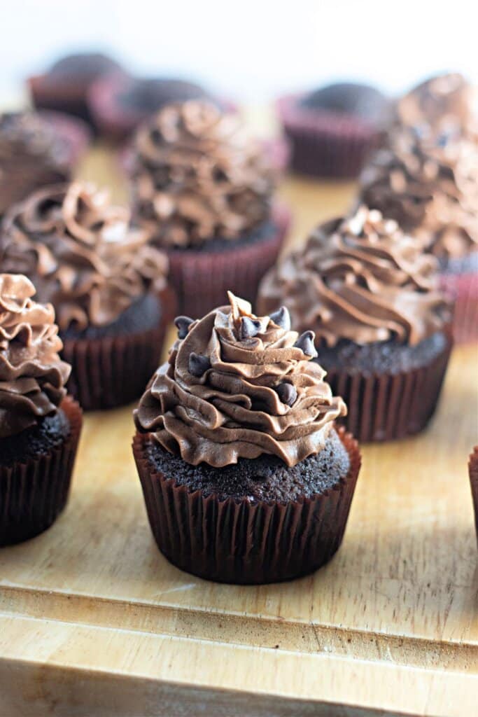 Chocolate buttercream cupcakes on a wooden cutting board.