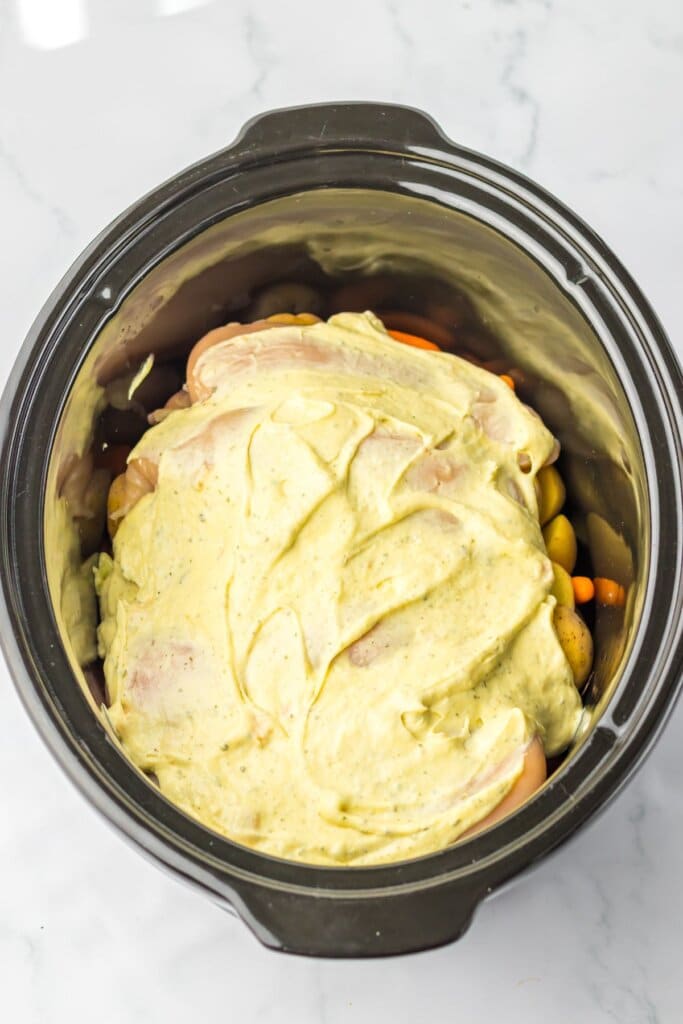 Soup being spread on top of vegetables in a slow cooker.