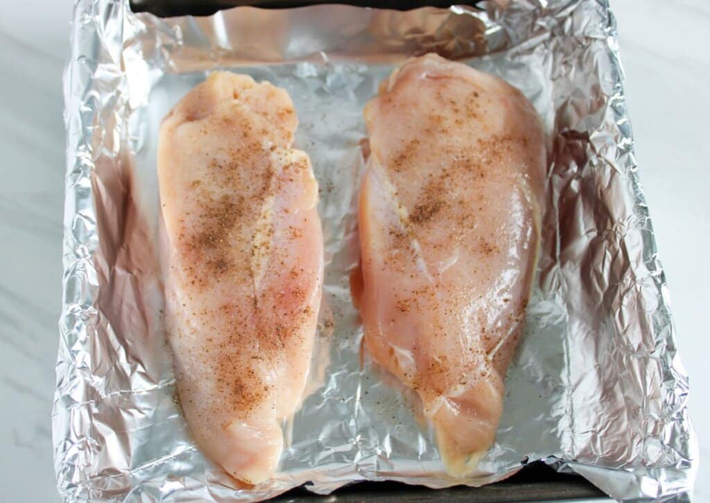 Salt and pepper sprinkled on a chicken breasts in a baking dish.