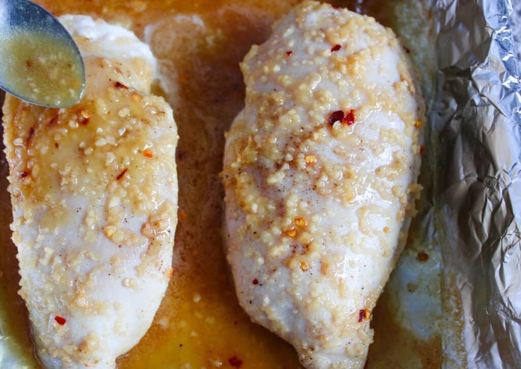 Sauce being spread on raw chicken in a baking dish.