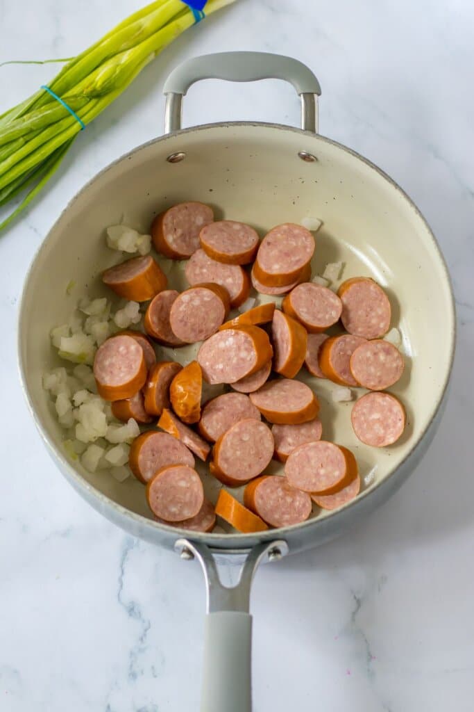 Smoked sausage and onions being cooked in a skillet.