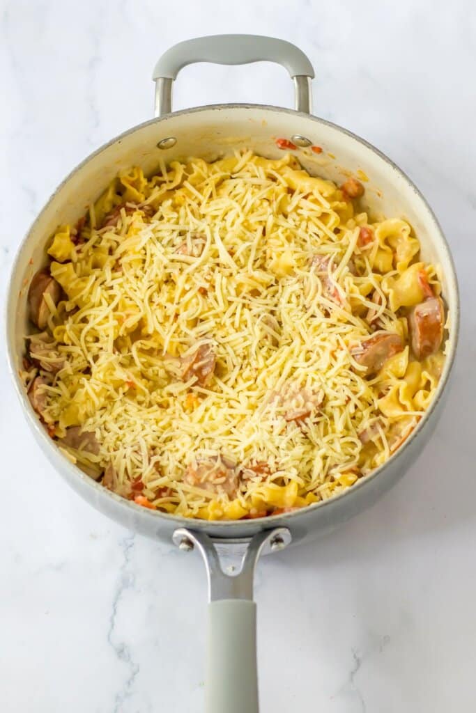 Shredded cheese being sprinkled on top of food in a skillet.