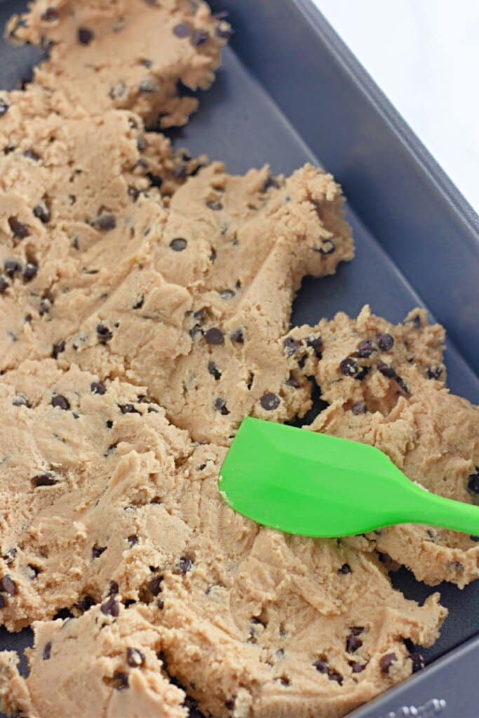 Cookie dough being spread in a metal pan.