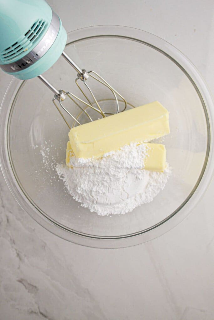 Butter and powdered sugar being mixed in a glass bowl.