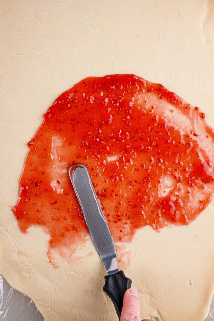 Jam being spread on top of dough.