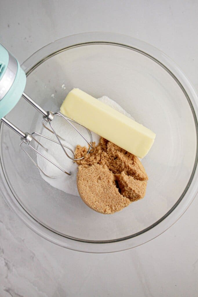 Butter, brown sugar, and granulated sugar being mixed in a glass bowl.