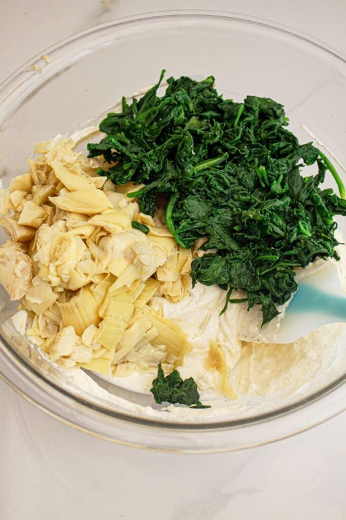 Spinach and artichokes being added to a large bowl.