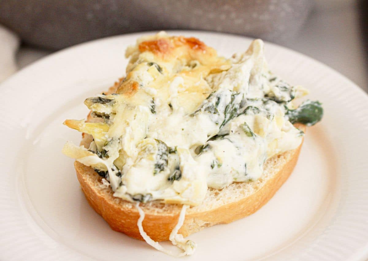 Spinach dip being spread on top of a piece of toast.