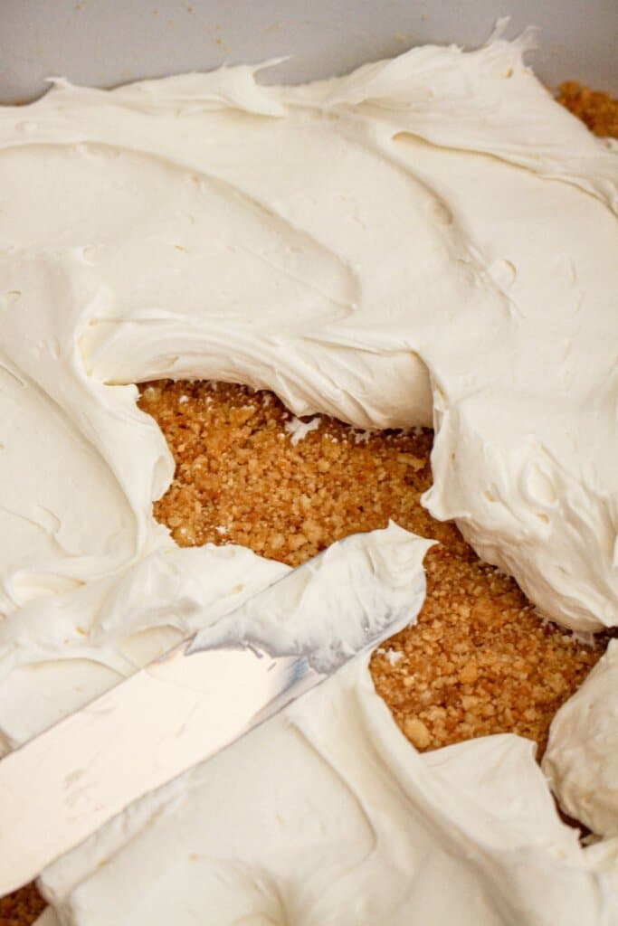 Cream cheese layer being spread on top of crust.