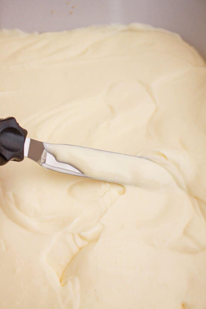 Cheesecake pudding being spread on top of a dessert.