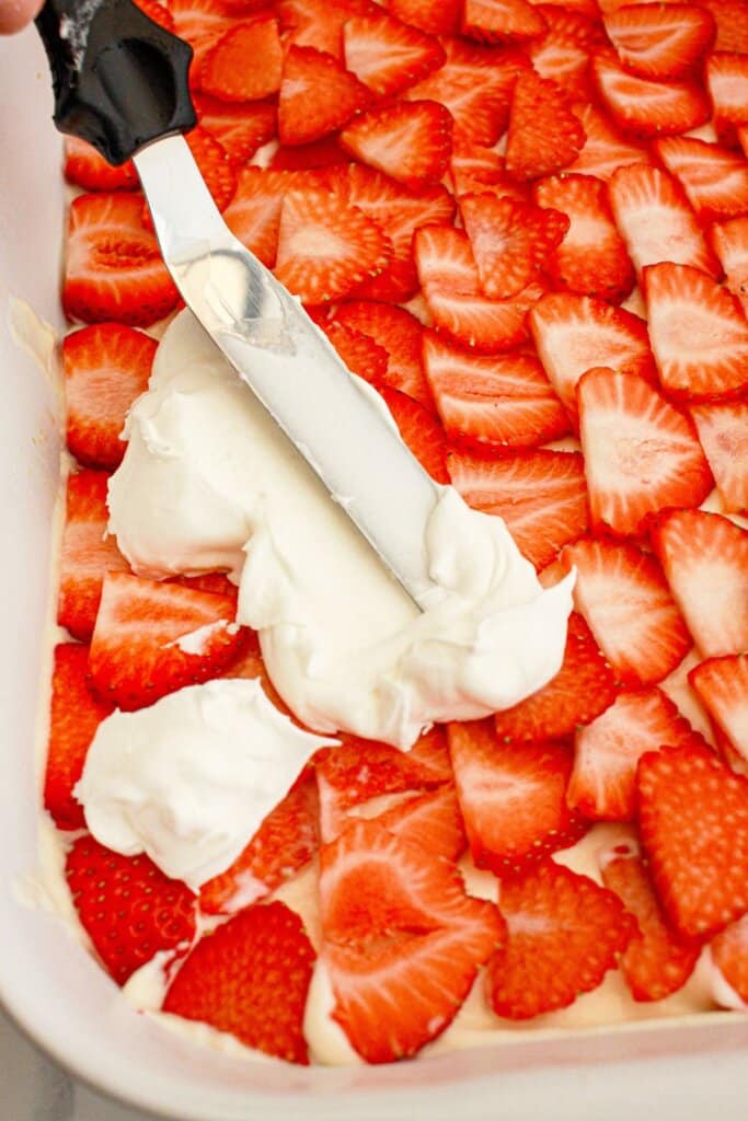 Cool Whop being spread on top of sliced strawberries.