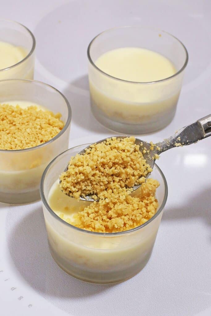 Graham cracker crumbs being sprinkled on top of dessert cups.