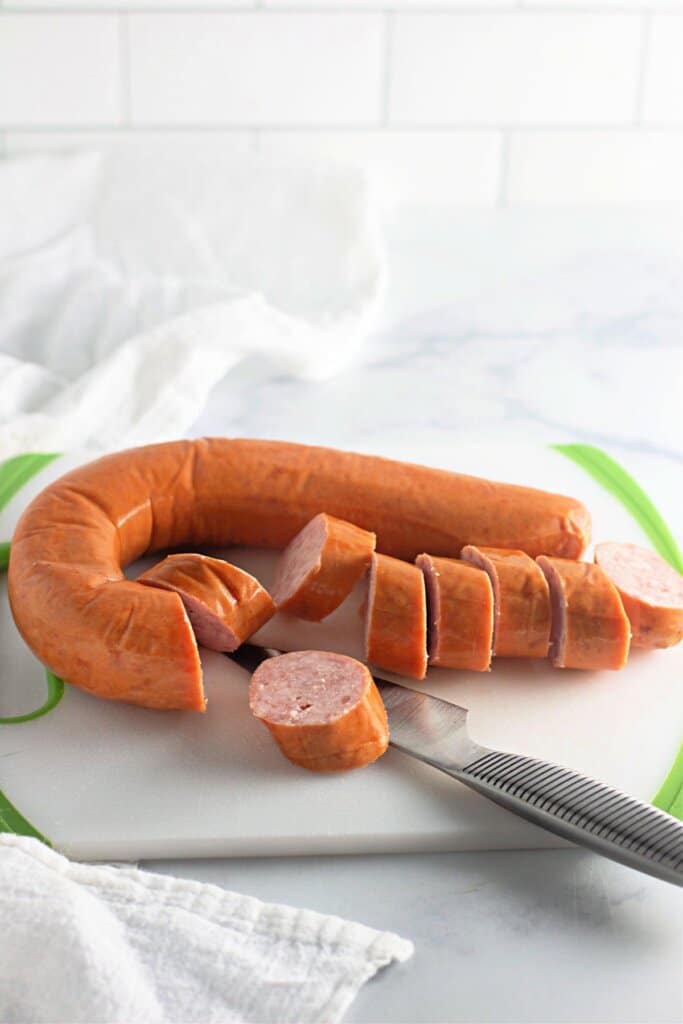 Smoked sausage being sliced on a cutting board.