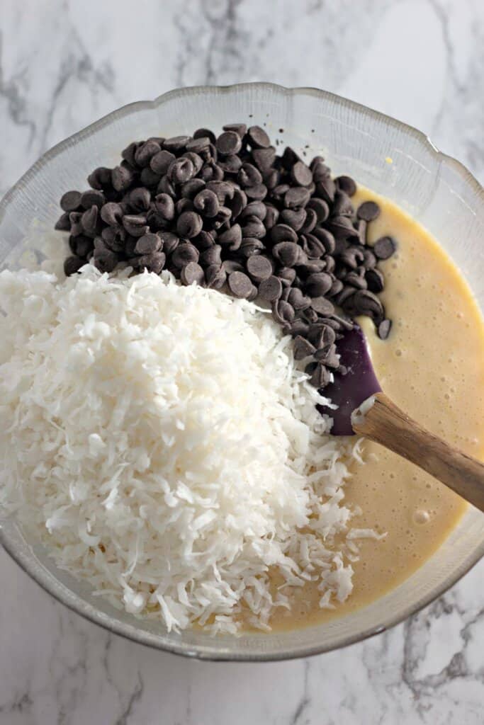 Chocolate chips being added to batter in a glass bowl.