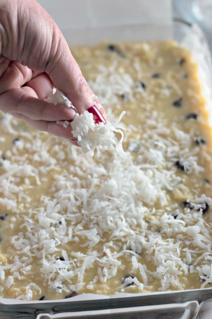 Coconut being sprinkled on top of batter in a baking dish.
