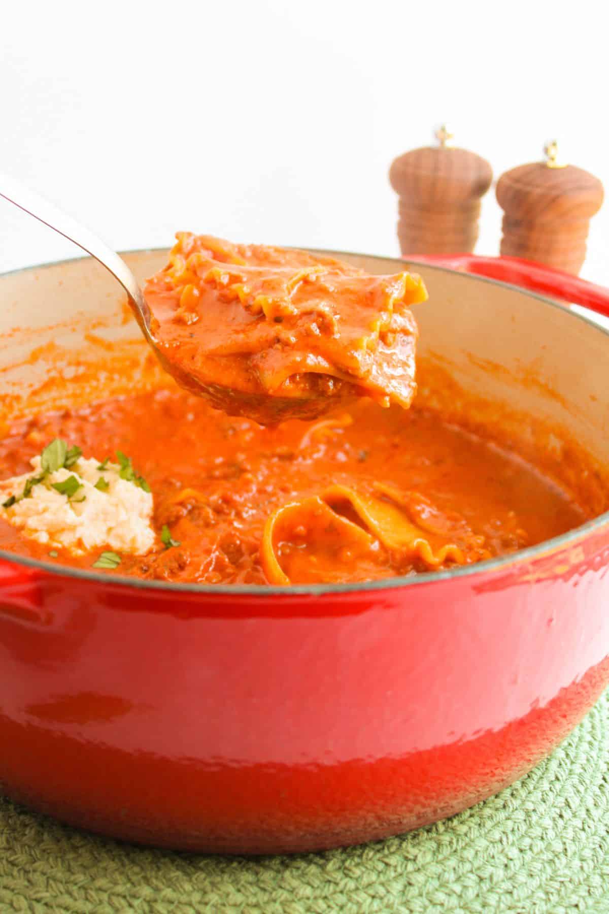 Spoonful of lasagna soup held in the air over a bowl.