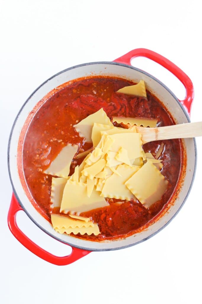 Noodles being added to a pot of meat sauce.