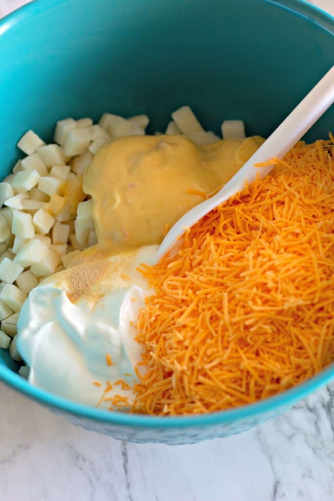 Potatoes, sour cream, and cheese being mixed together in a bowl.