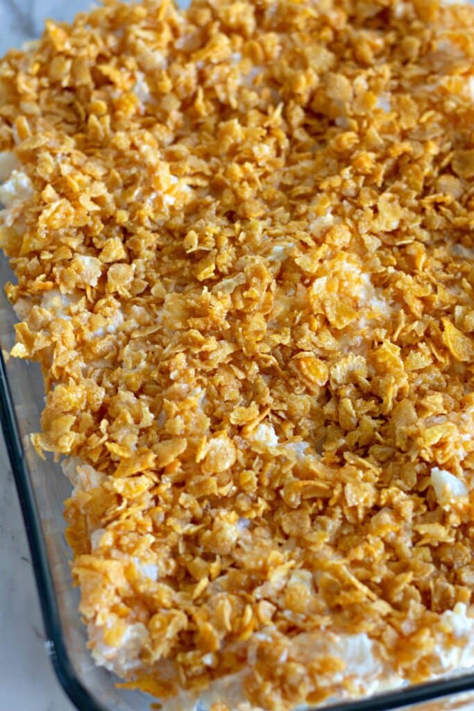 Cornflakes being sprinkled on top of a cassserole.