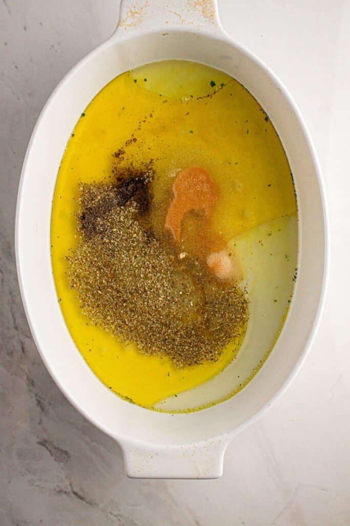 Olive oil, broth, and seasonings in a white baking dish.