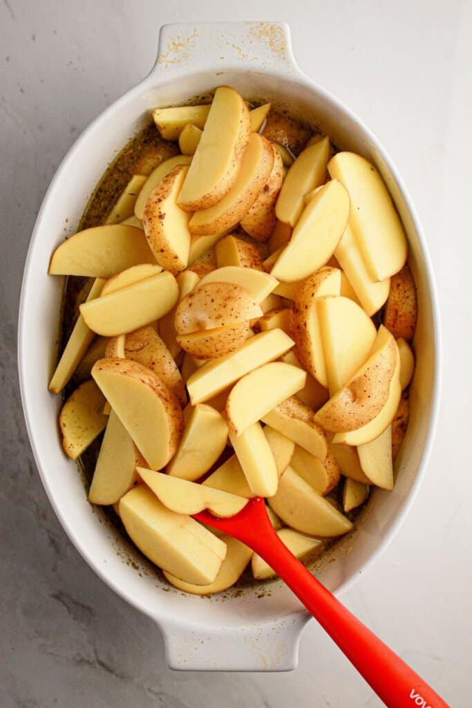 Potatoes being added to a white baking dish.