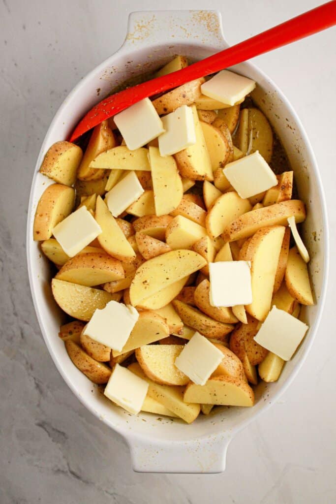 Butter slices on top of potatoes in a baking dish.