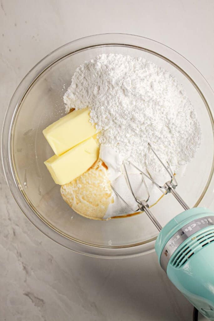 Powdered sugar and butter being mixed in a glass mixing bowl.