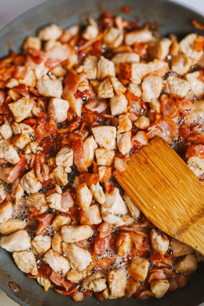Chicken and bacon being cooked in a large skillet.
