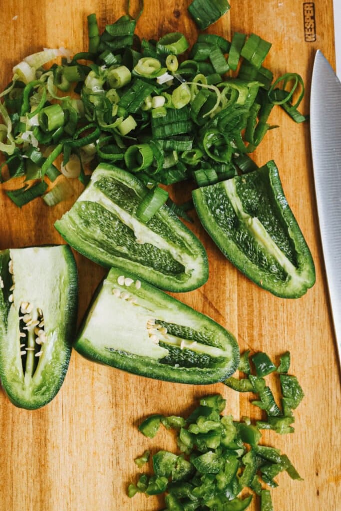 Peppers and green onions being cut on a cutting board.