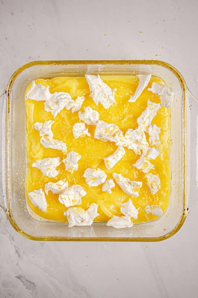 Cream cheese on top of lemon pie filling in a glass baking dish.
