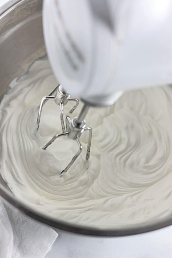Whipped cream being mixed in a stand mixer.