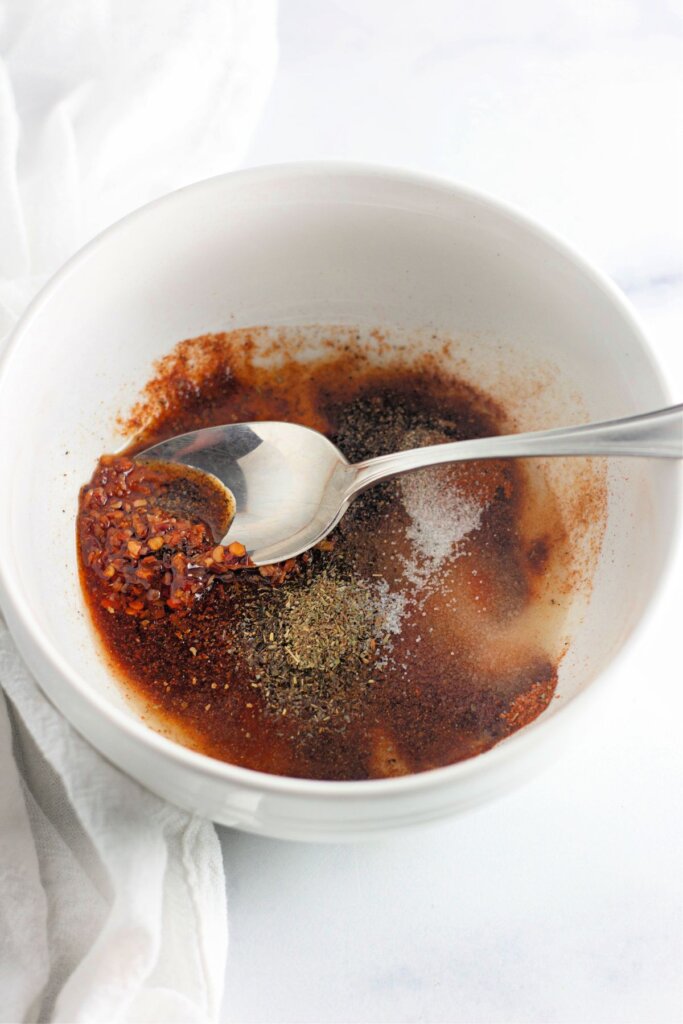 Seasonings and melted butter being mixed with a spoon in a small bowl.