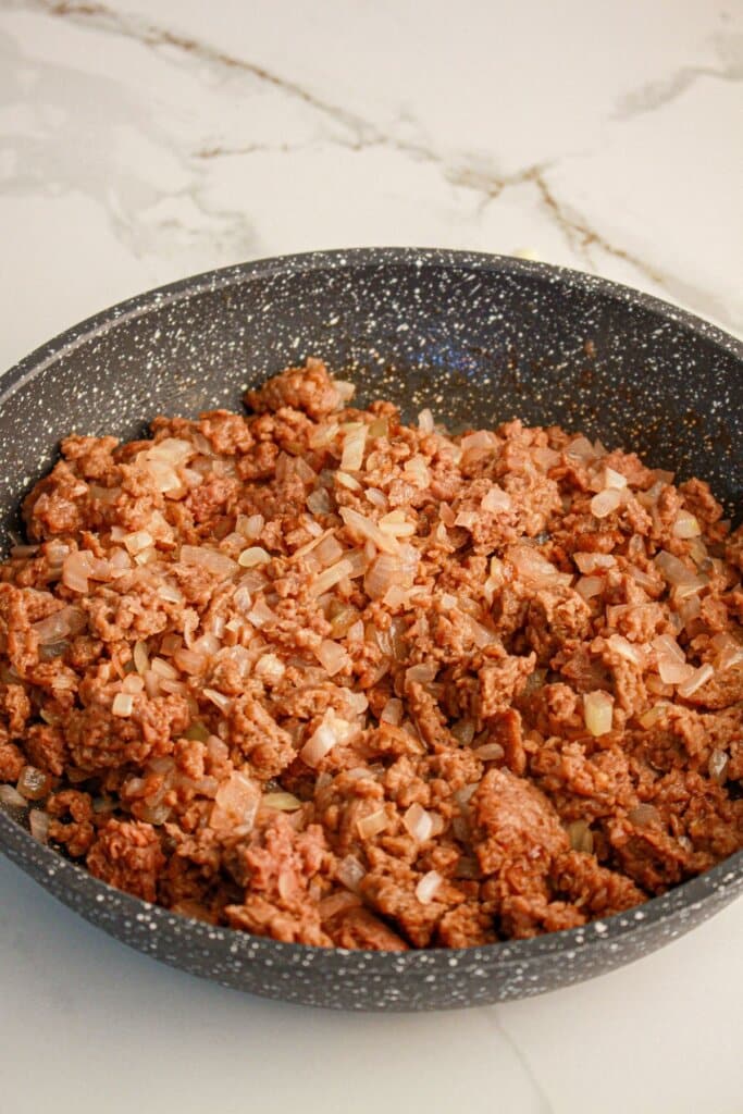 Ground beef and onions being cooked in a skillet.