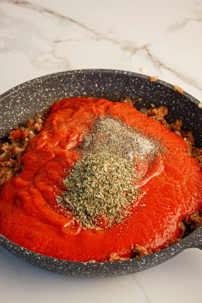 Sauce and seasonings being added to a skillet.