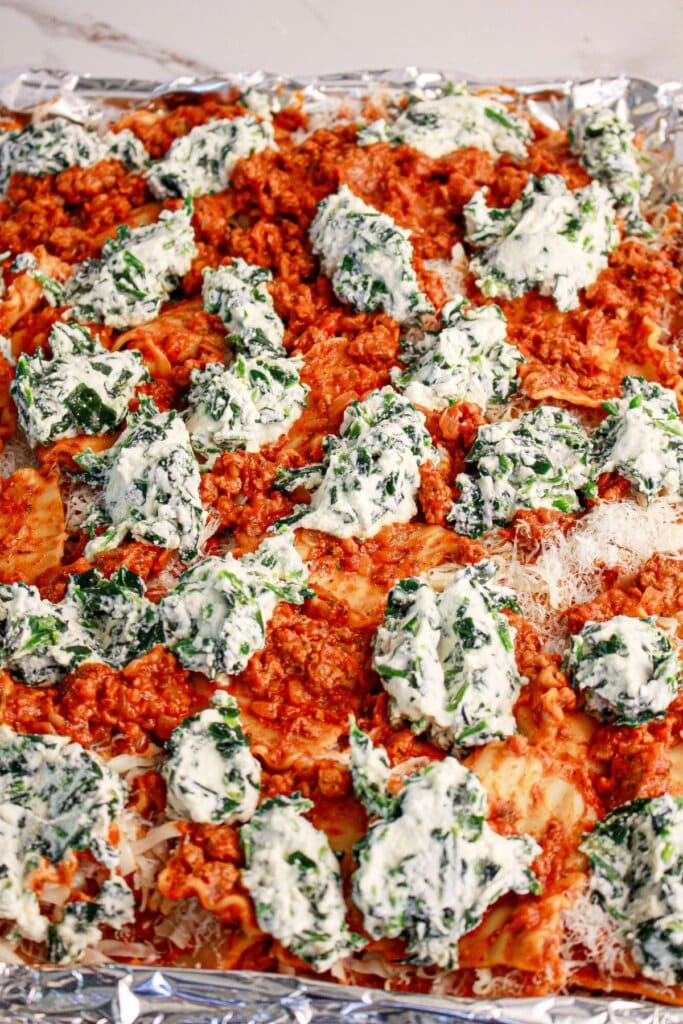 Ricotta and spinach being dolloped on top of pasta.