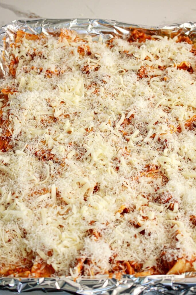 Cheese on top of pasta in a baking sheet.