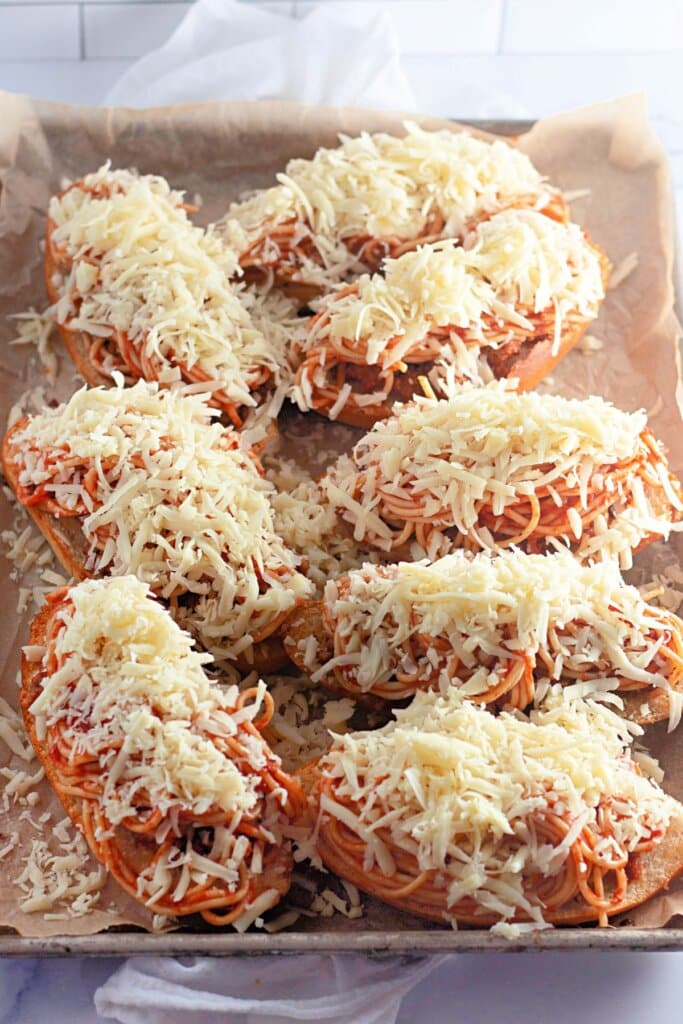 Cheese being sprinkled on top of a bread on a baking sheet.
