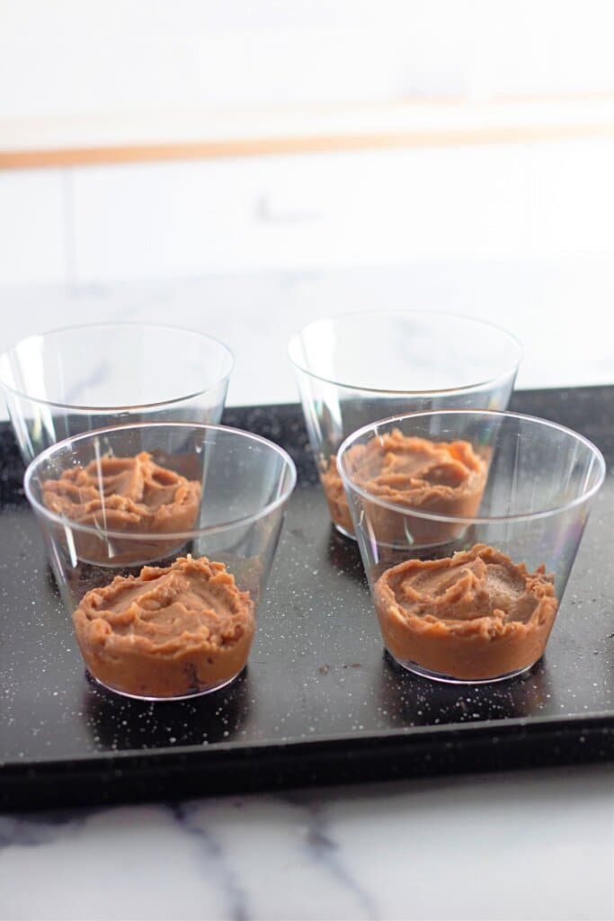 Refried beans being spread into small bowls.