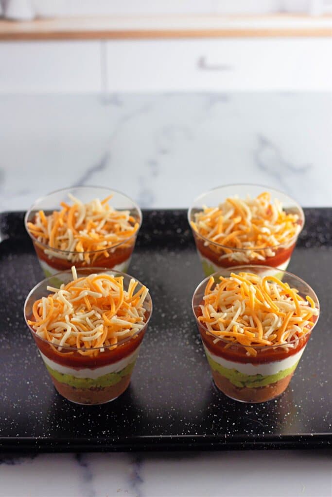 Shredded cheese being sprinkled on top of salsa in cups.