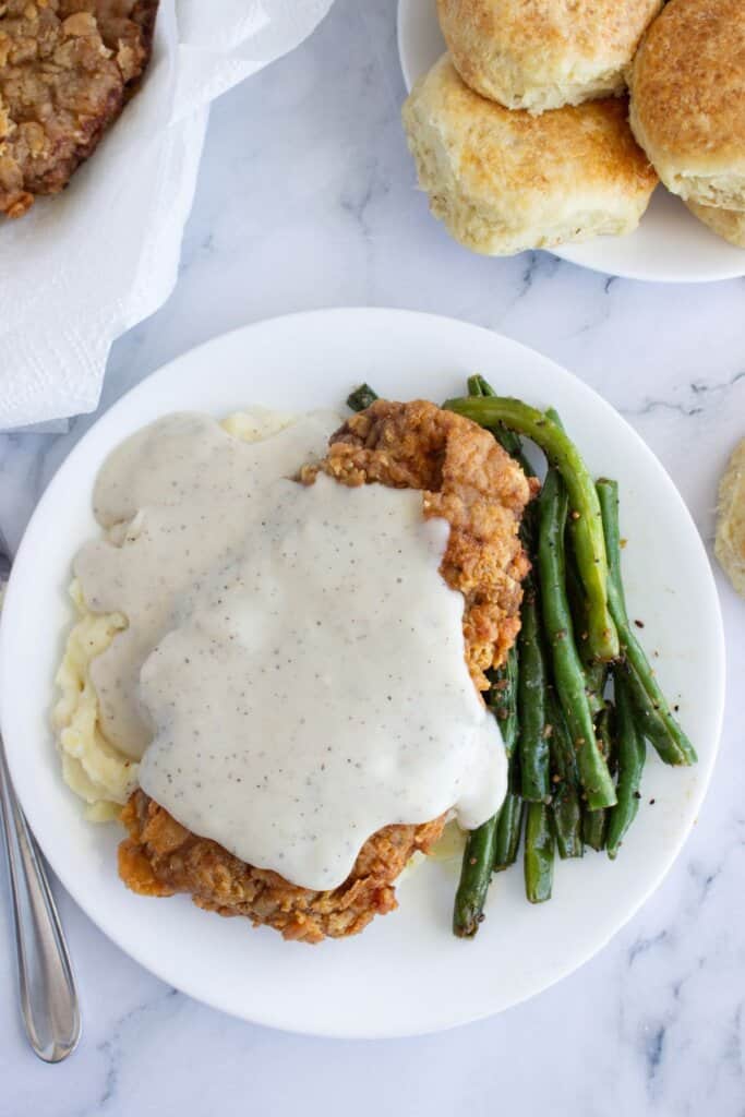 Chicken fried steak, green beans, and mashed potatoes on a plate.