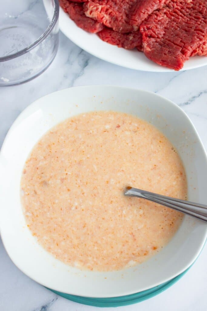 Egg and hot sauce being mixed in a small white bowl.